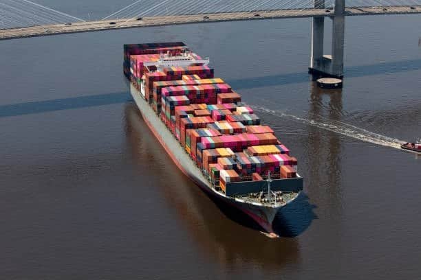 Container ship carrying stacked cargo containers, representing international freight shipping and drayage connection to inland transport.