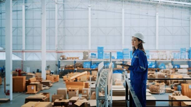 Female worker in warehouse managing logistics operations with clipboard.