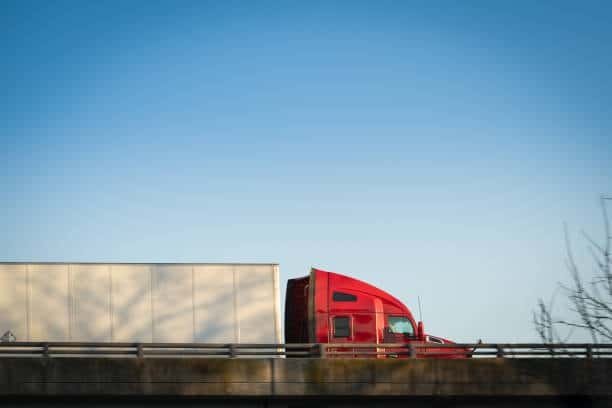 Red transport truck on highway carrying e-commerce goods.