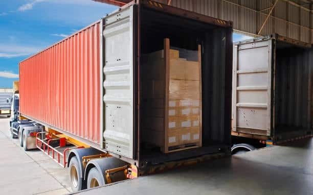 “Red FCL shipping container on truck trailer fully packed with cargo pallets”
