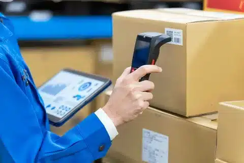 “Warehouse staff scanning package barcode with handheld scanner and tablet during fulfillment process”