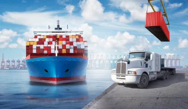 Drayage truck waiting as container is loaded beside container ship, highlighting port drayage operations.