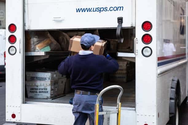 USPS mail carrier placing packages inside postal delivery vehicle.