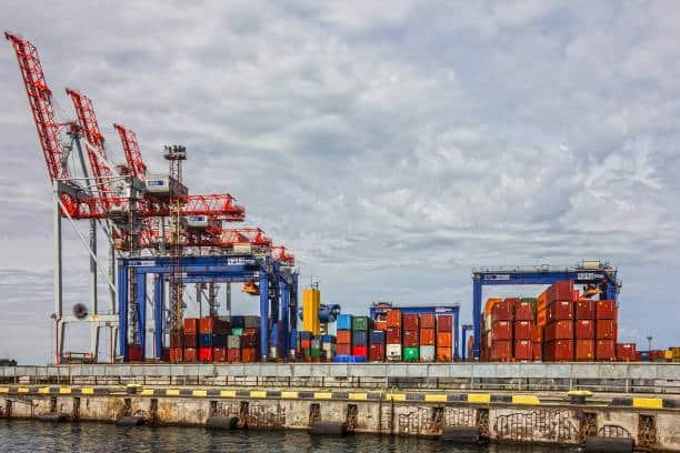 Container cranes loading and unloading vessels, illustrating origin and destination THC costs.